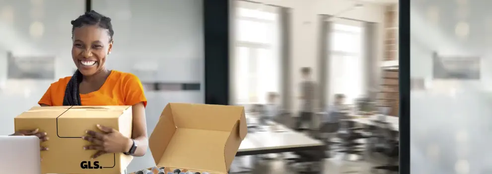 Une femme souriante tenant un colis GLS dans un bureau.