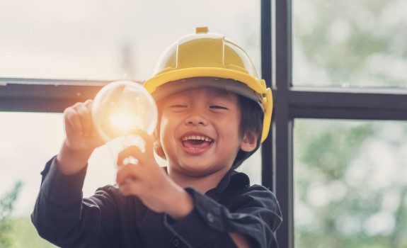 A child wearing a safety helmet holds a light bulb. A child wearing a safety helmet holds a light bulb.