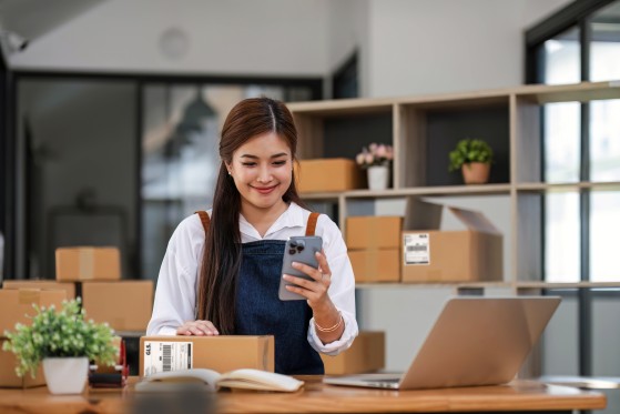 Customer preparing GLS shipments with a smartphone in hand and a laptop on her desk.